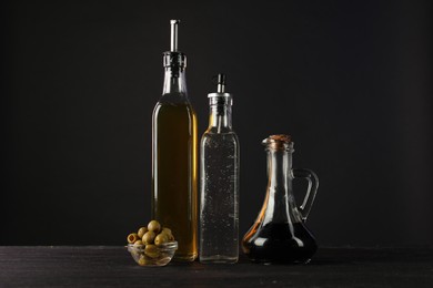 Photo of Salad dressings and olives on wooden table against black background