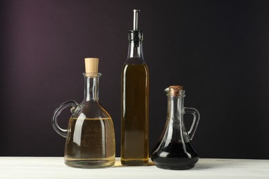 Photo of Oil and vinegar in bottles on white wooden table against dark background