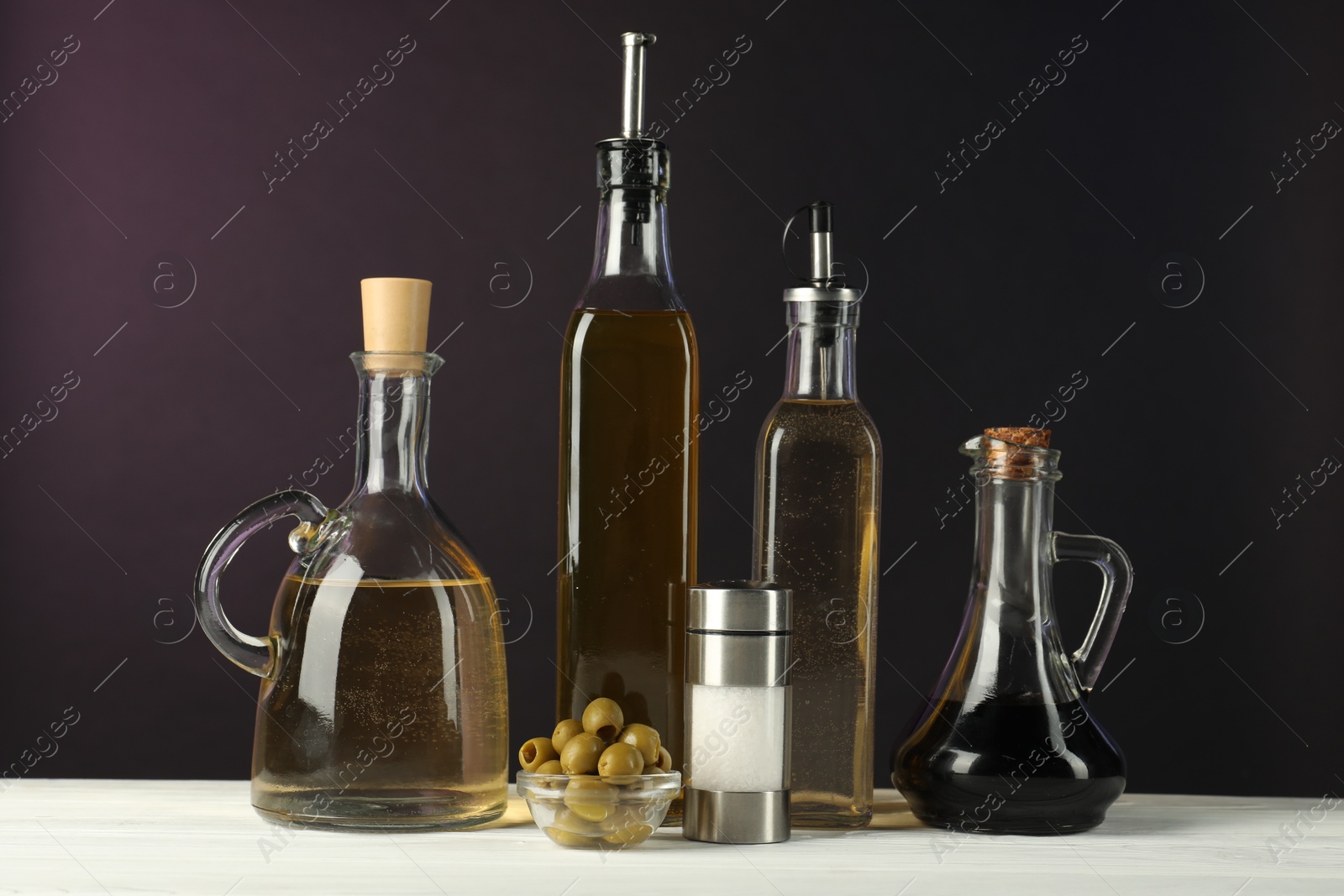 Photo of Salad dressings, olives and salt on white wooden table against dark background