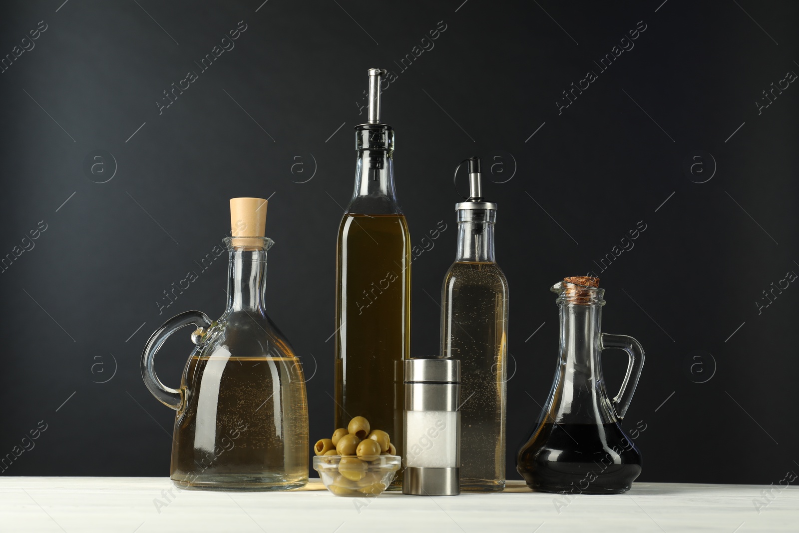 Photo of Salad dressings, olives and salt on white wooden table against black background