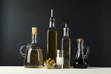 Photo of Salad dressings, olives and salt on white wooden table against black background