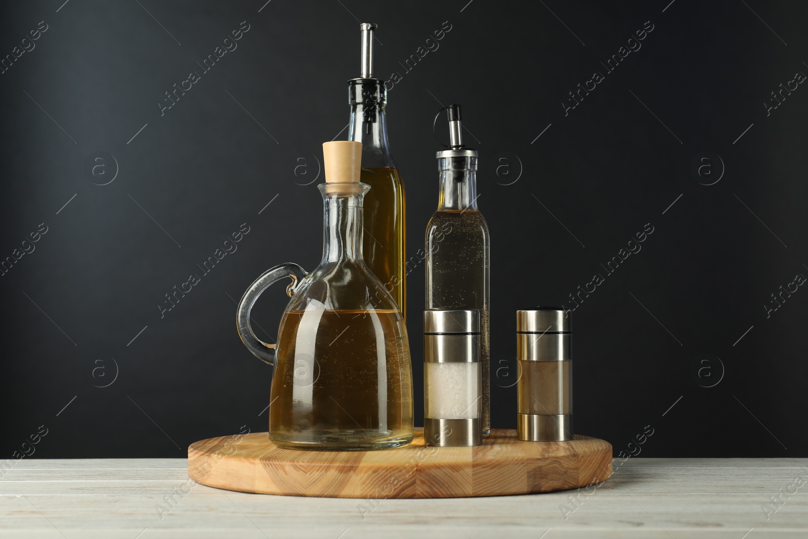 Photo of Salad dressings and spices on white wooden table against black background