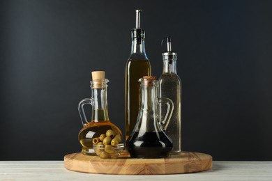 Photo of Salad dressings and olives on white wooden table against black background