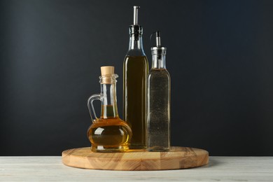 Photo of Oils and vinegar in bottles on white wooden table against black background