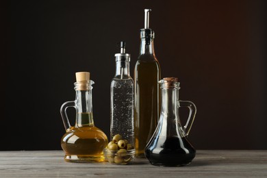 Photo of Salad dressings and olives on wooden table against dark background