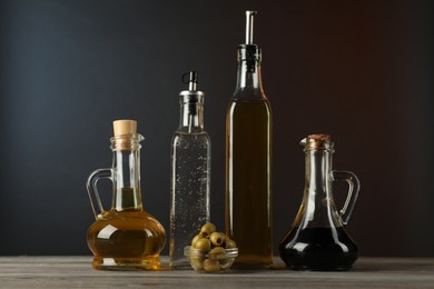 Photo of Salad dressings and olives on wooden table against dark background