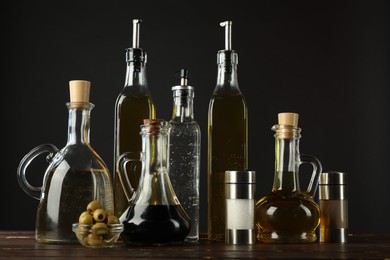 Photo of Salad dressings, olives and spices on wooden table against black background