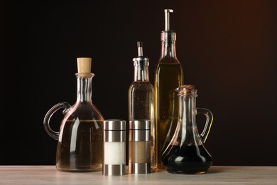 Photo of Salad dressings and spices on wooden table against dark background