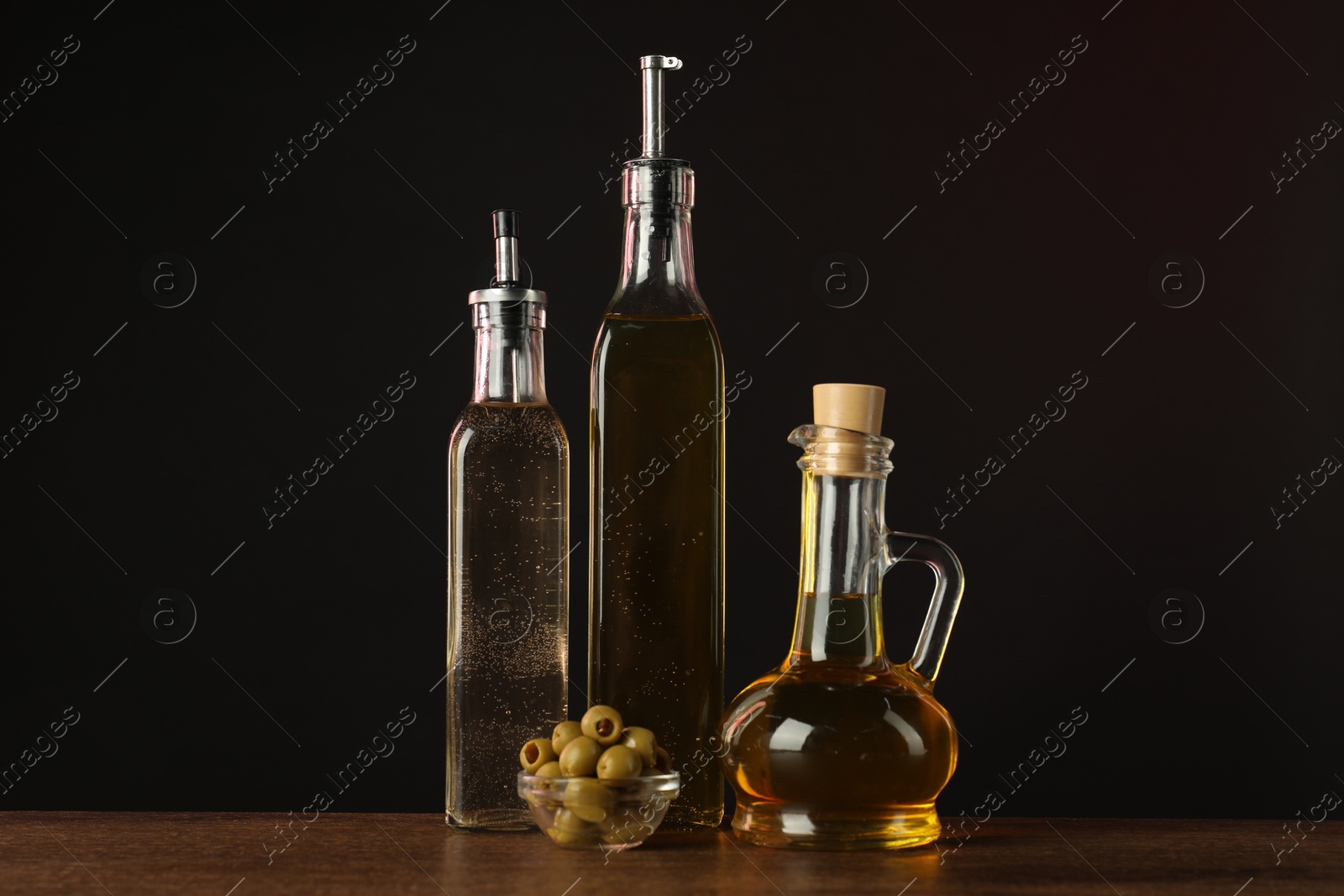 Photo of Salad dressings and olives on wooden table against dark background