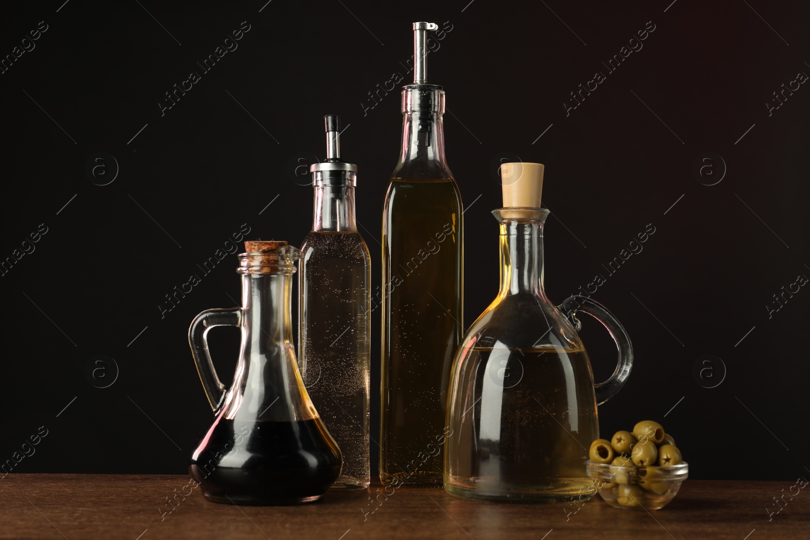 Photo of Salad dressings and olives on wooden table against dark background