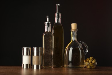 Photo of Salad dressings, spices and olives on wooden table against dark background