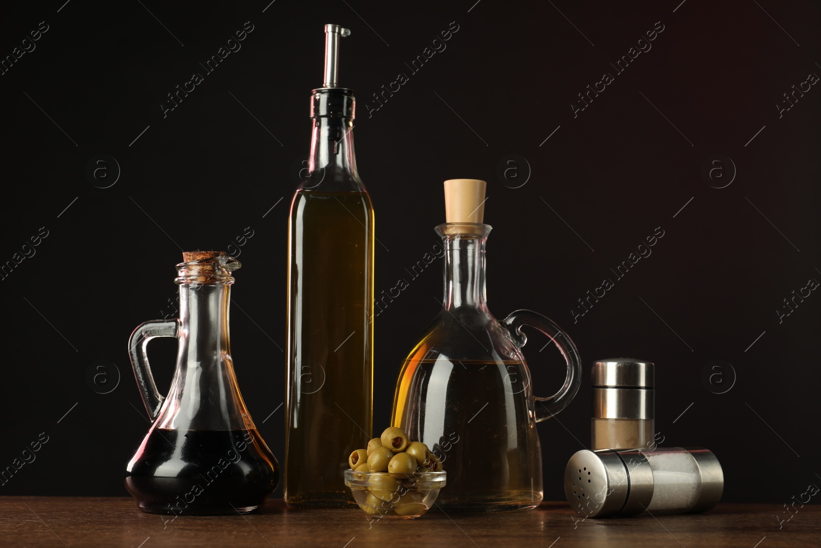 Photo of Salad dressings, spices and olives on wooden table against dark background