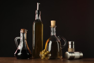 Photo of Salad dressings, spices and olives on wooden table against dark background