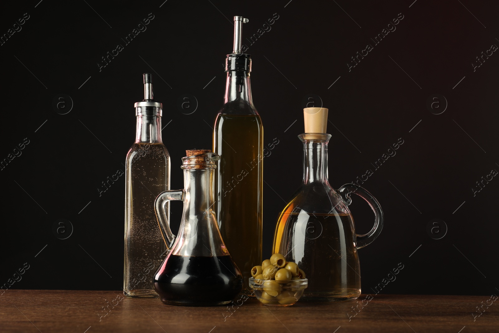 Photo of Salad dressings and olives on wooden table against dark background