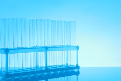 Photo of Empty test tubes on mirror surface against light blue background, space for text. Laboratory glassware