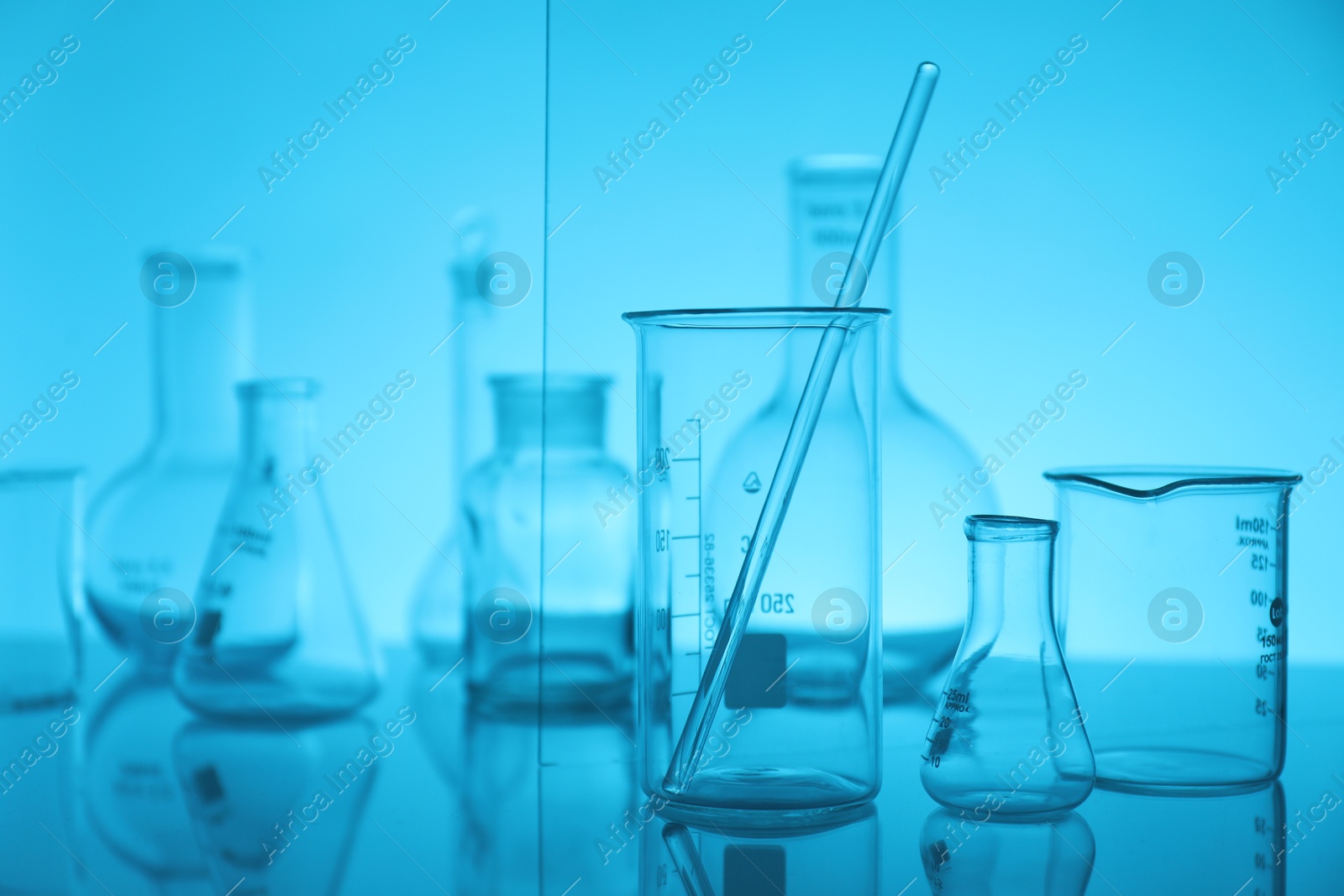 Photo of Laboratory glassware on mirror surface against light blue background