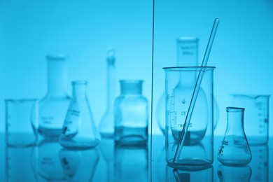 Photo of Laboratory glassware on mirror surface against light blue background