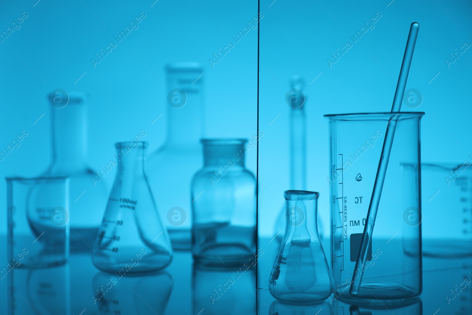 Photo of Laboratory glassware on mirror surface against light blue background