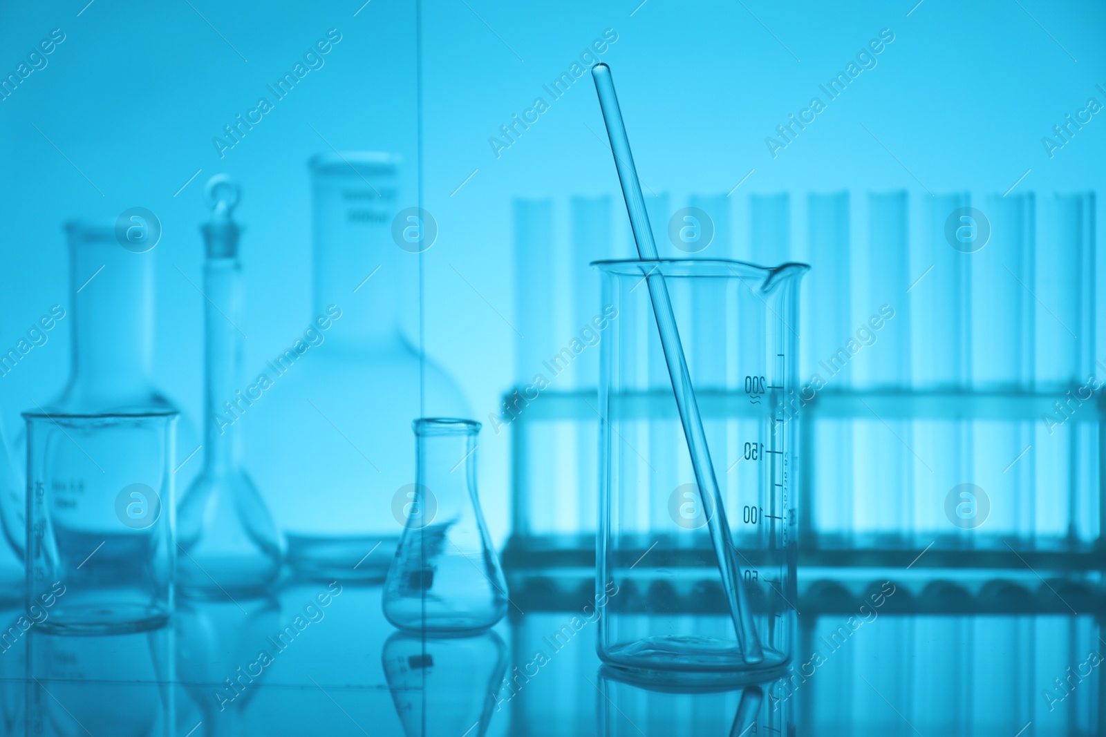 Photo of Laboratory glassware on mirror surface against light blue background