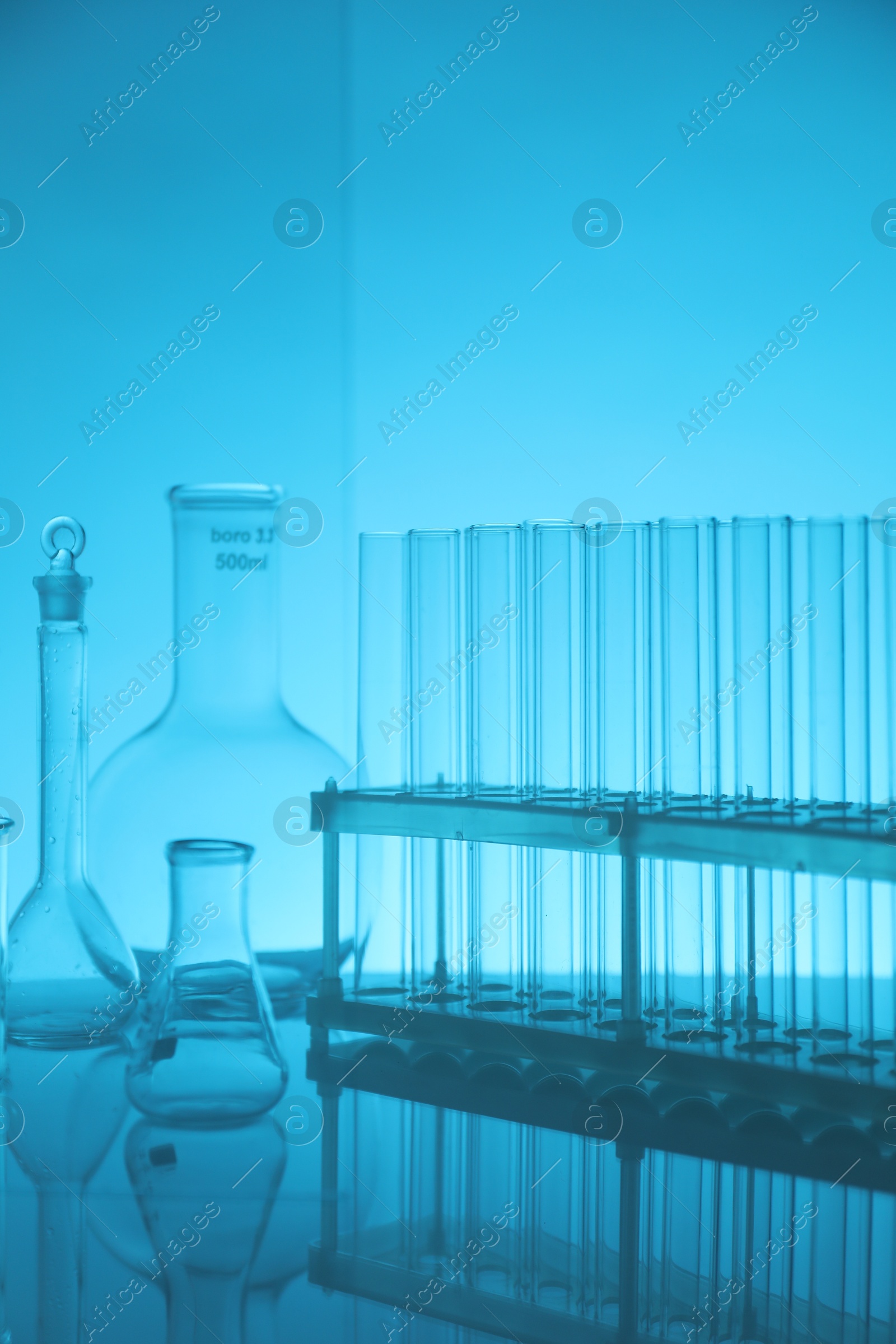 Photo of Laboratory glassware on mirror surface against light blue background