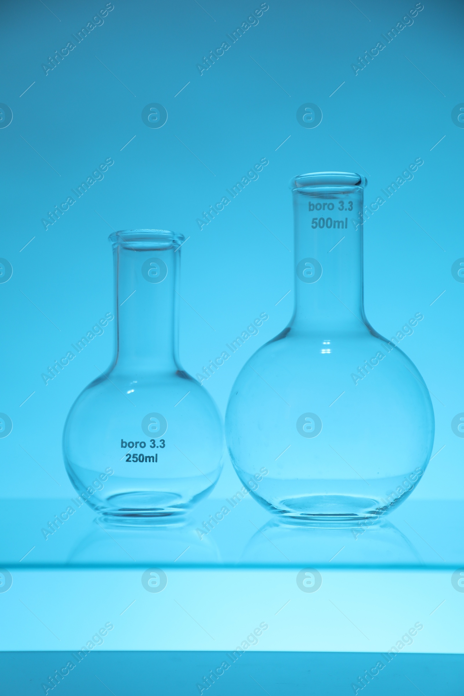 Photo of Empty flasks on light blue background. Laboratory equipment