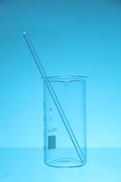 Photo of Beaker and rod on light blue background. Laboratory equipment