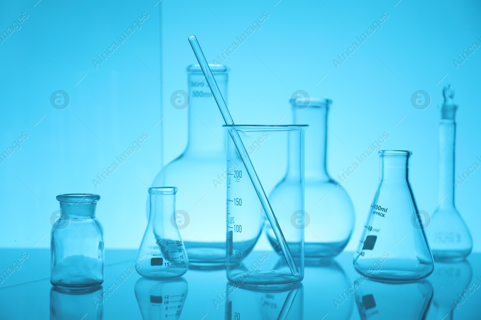 Photo of Laboratory glassware on mirror surface against light blue background