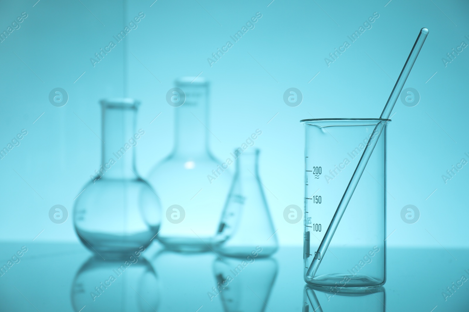 Photo of Laboratory glassware on mirror surface against light blue background