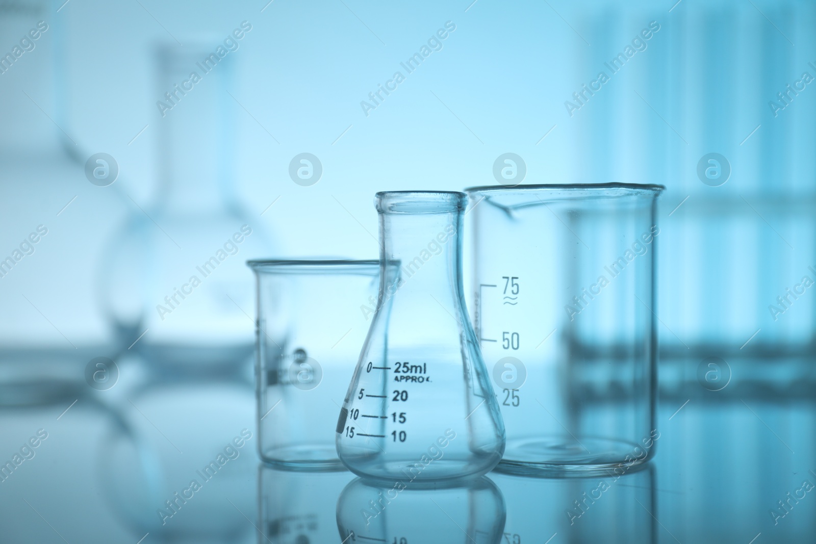 Photo of Laboratory glassware on mirror surface against light blue background