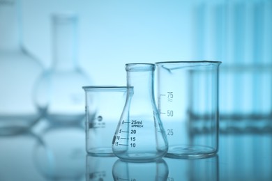 Photo of Laboratory glassware on mirror surface against light blue background