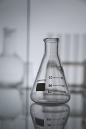 Photo of Empty flask on mirror surface against light background. Laboratory equipment