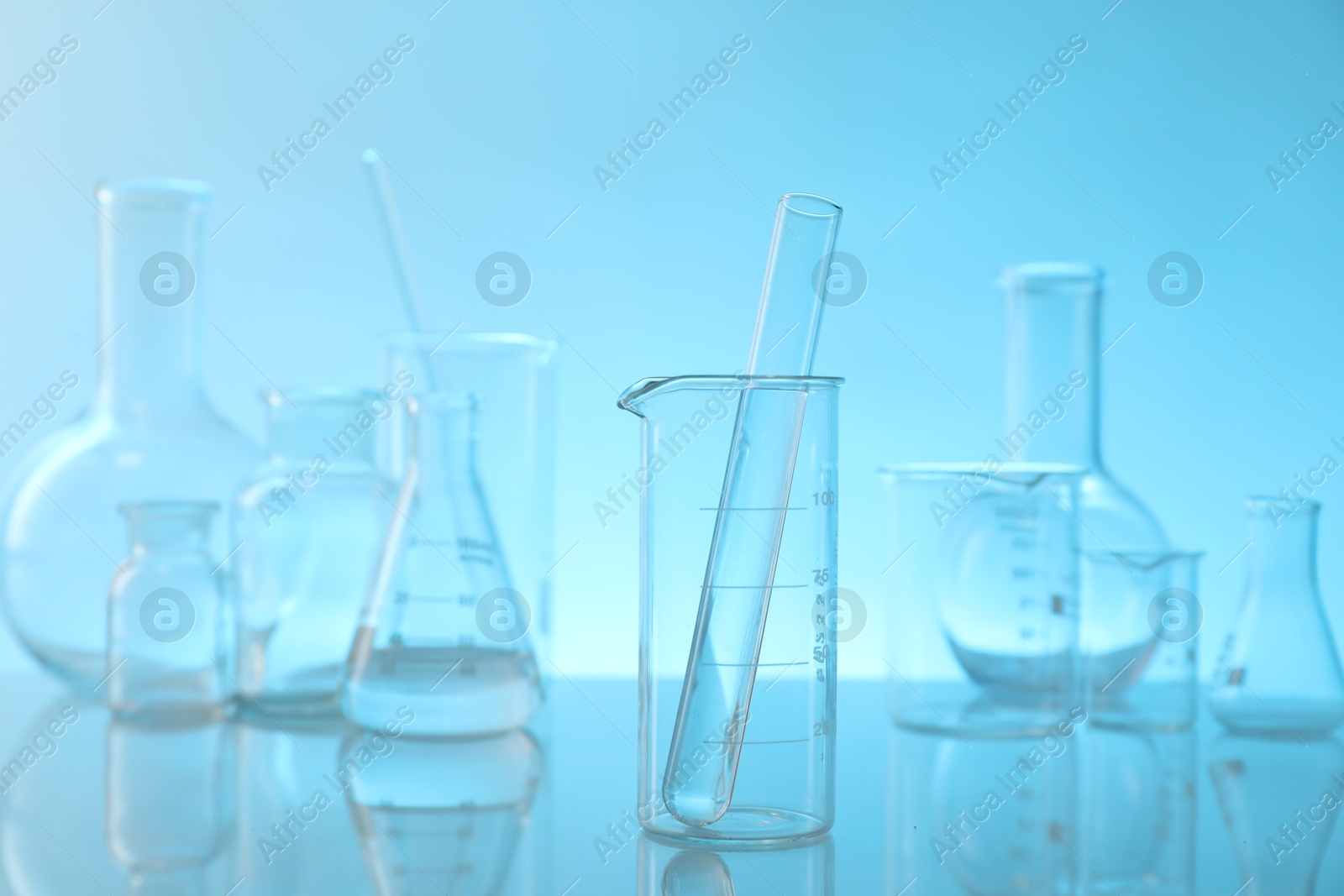 Photo of Laboratory glassware on mirror surface against light blue background