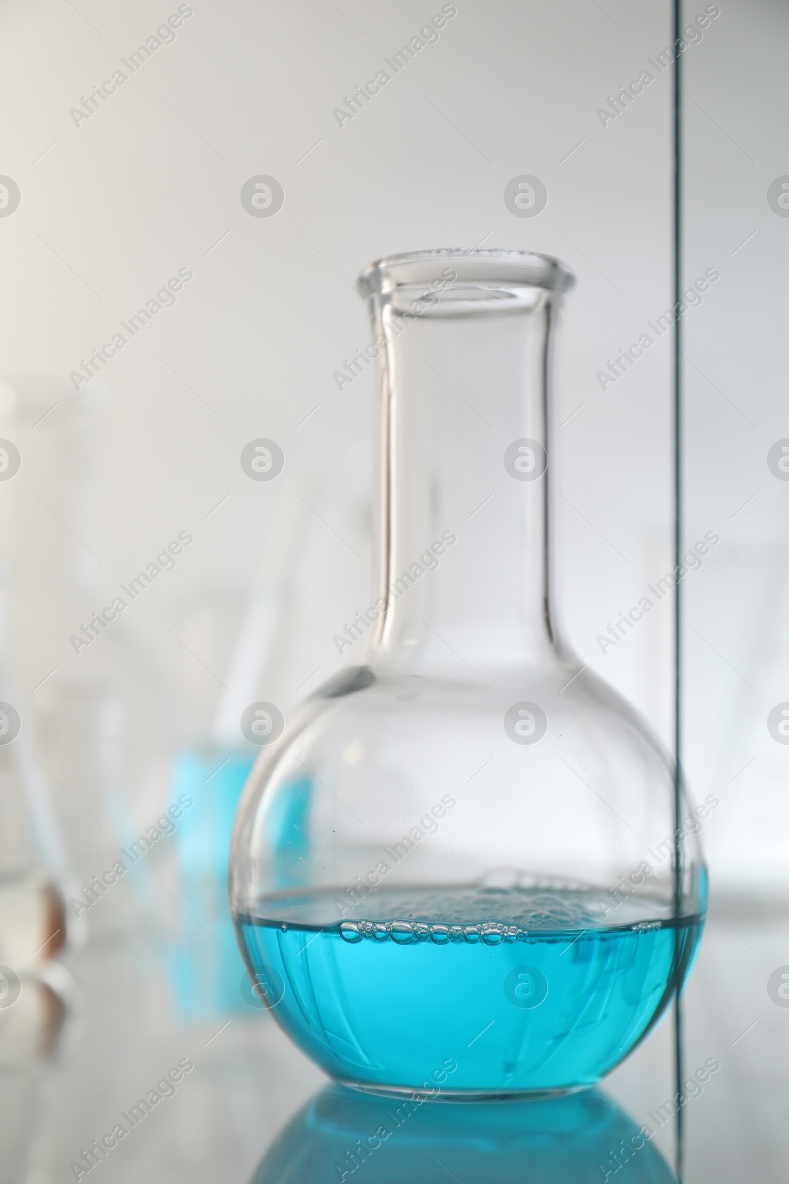 Photo of Flask with liquid on mirror surface against light background. Laboratory glassware