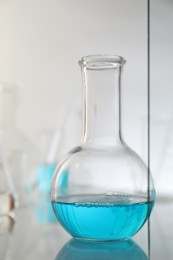 Photo of Flask with liquid on mirror surface against light background. Laboratory glassware