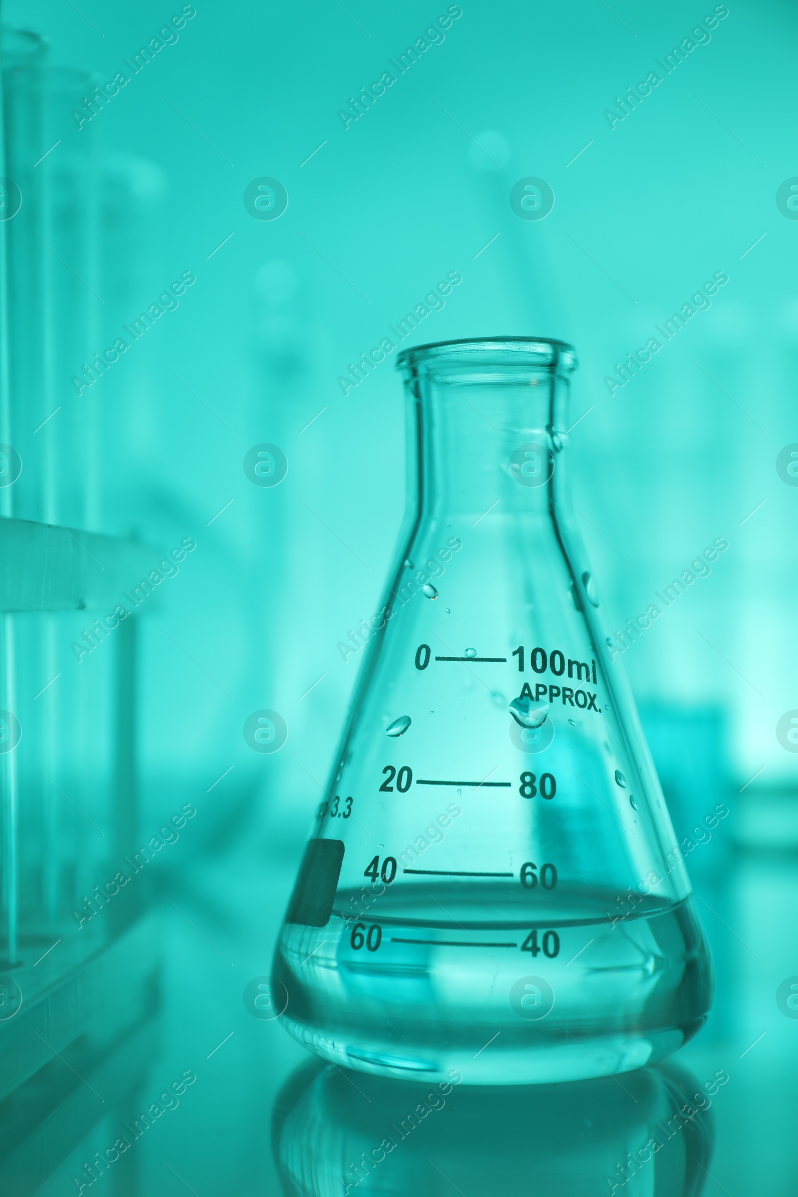 Photo of Flask with liquid on mirror surface against turquoise background. Laboratory glassware