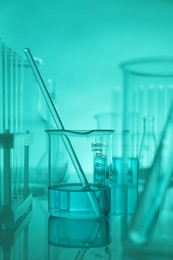 Photo of Laboratory glassware on mirror surface against turquoise background