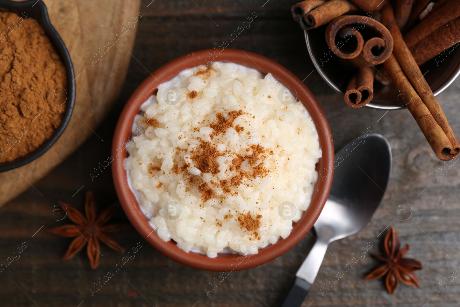 Photo of Tasty rice pudding with cinnamon served on wooden table, flat lay