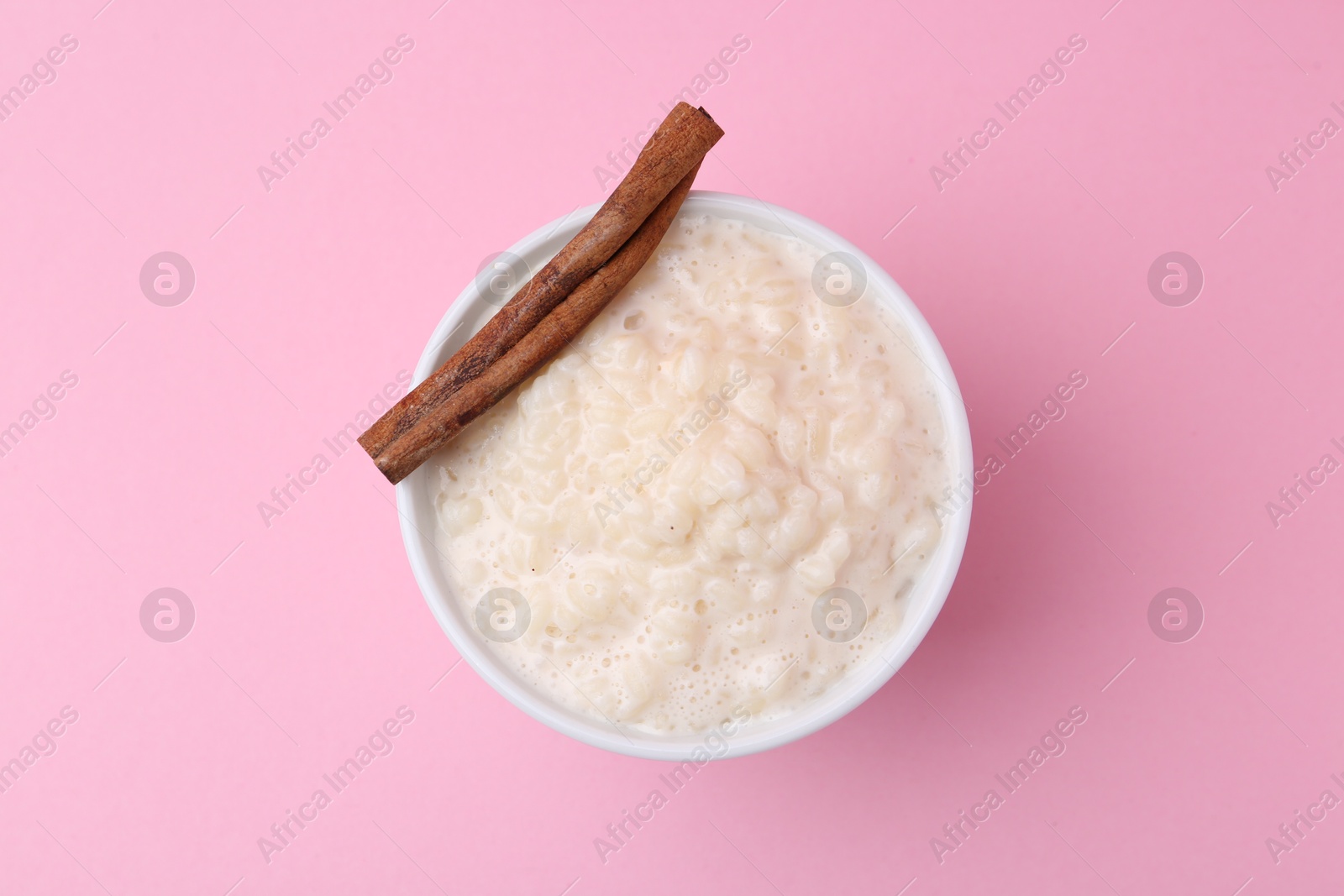 Photo of Tasty rice pudding with cinnamon on pink background, top view