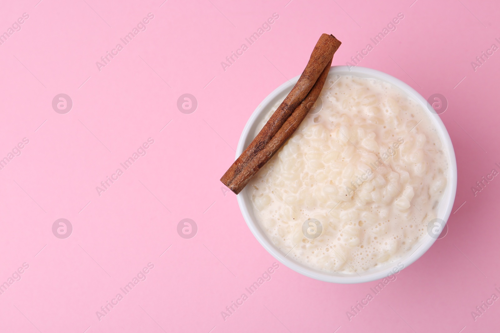 Photo of Tasty rice pudding with cinnamon on pink background, top view. Space for text