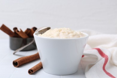 Photo of Tasty rice pudding with cinnamon served on white tiled table, closeup