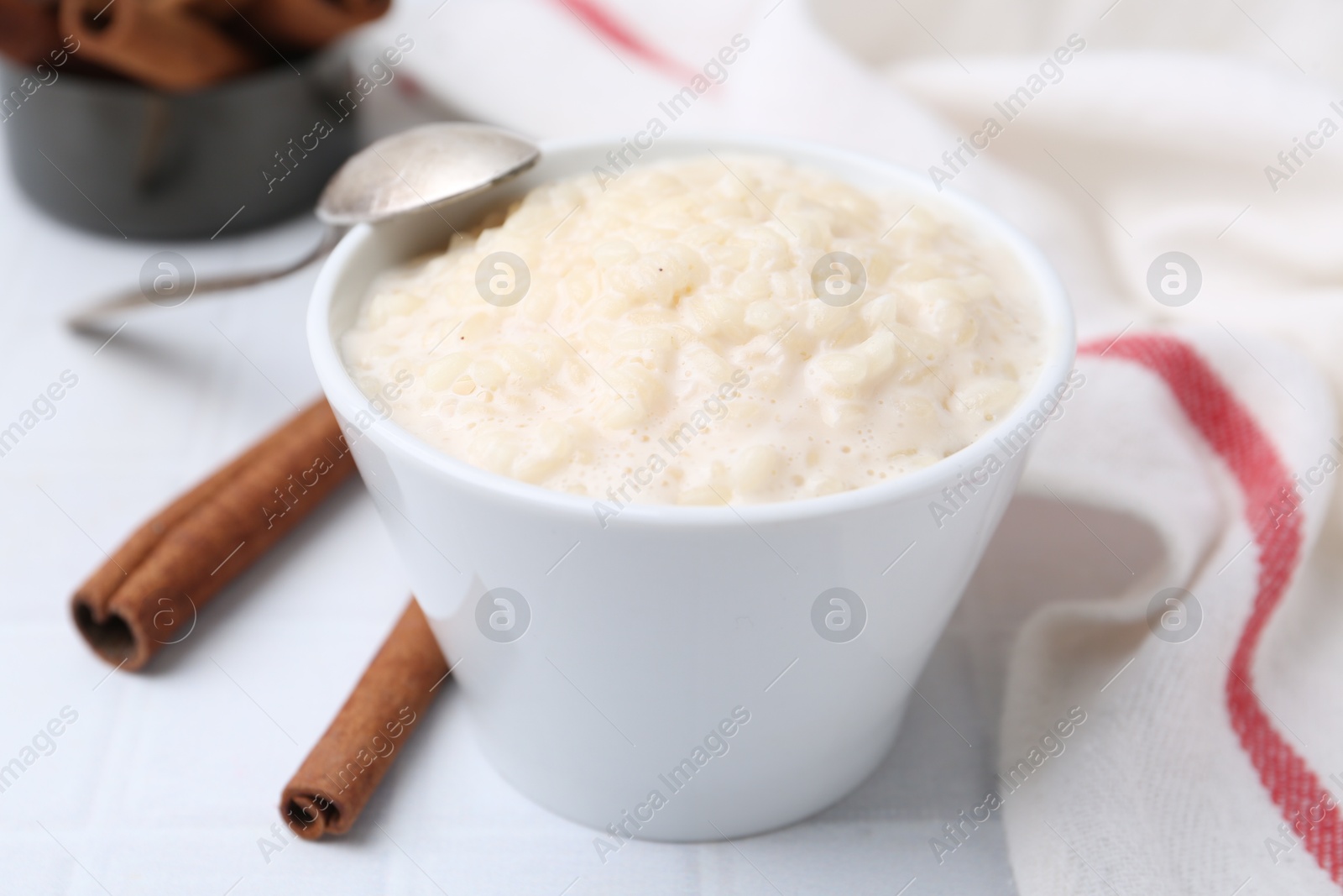 Photo of Tasty rice pudding with cinnamon served on white tiled table, closeup