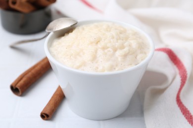 Photo of Tasty rice pudding with cinnamon served on white tiled table, closeup