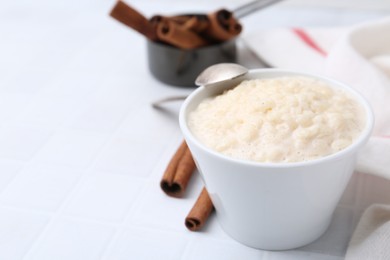 Photo of Tasty rice pudding with cinnamon served on white tiled table, closeup. Space for text