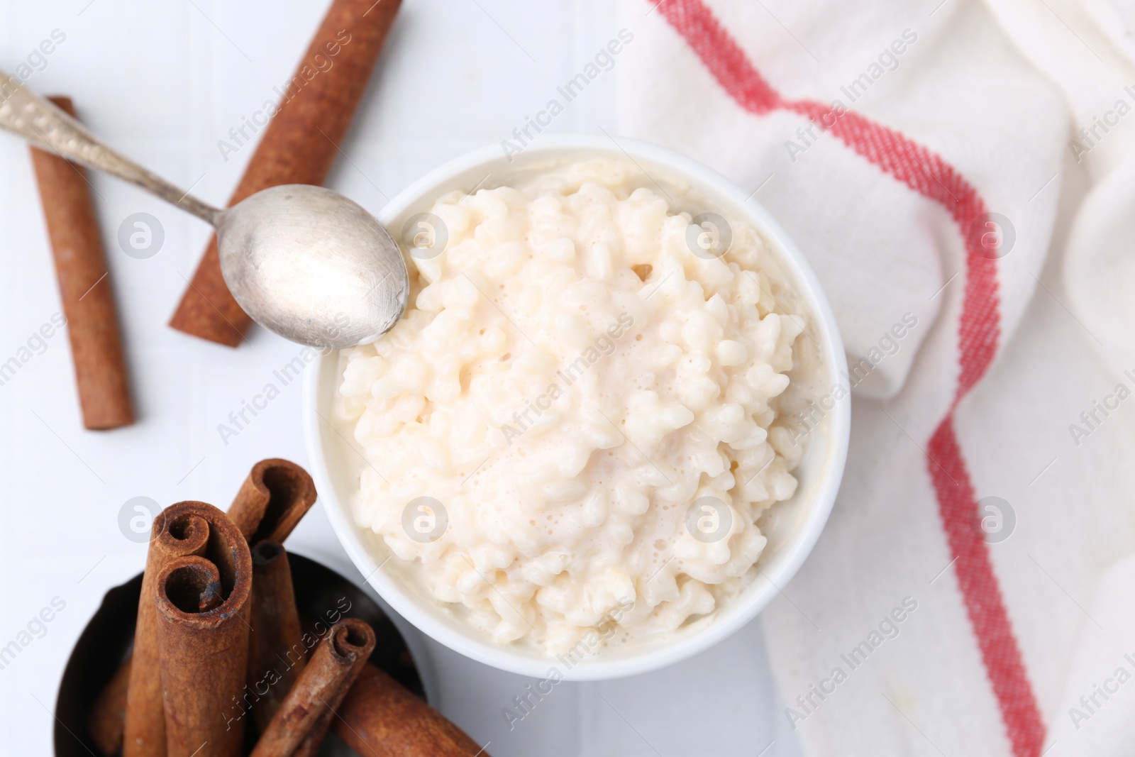 Photo of Tasty rice pudding with cinnamon served on white tiled table, flat lay