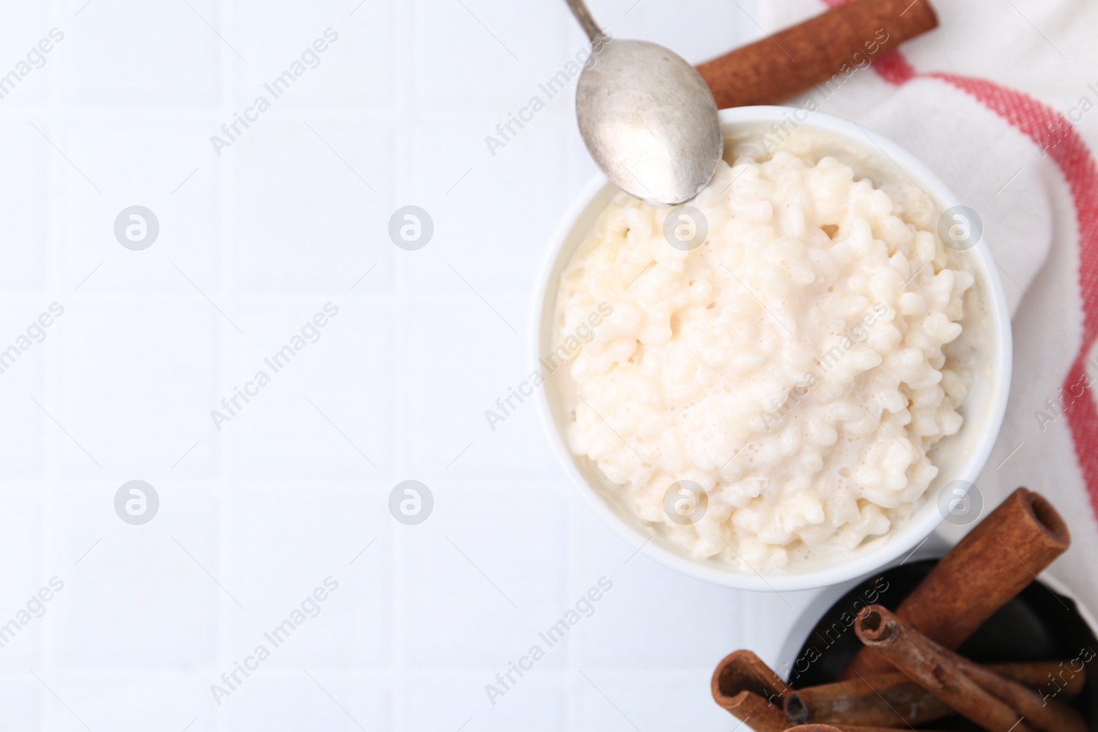 Photo of Tasty rice pudding with cinnamon served on white tiled table, flat lay. Space for text