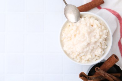 Photo of Tasty rice pudding with cinnamon served on white tiled table, flat lay. Space for text