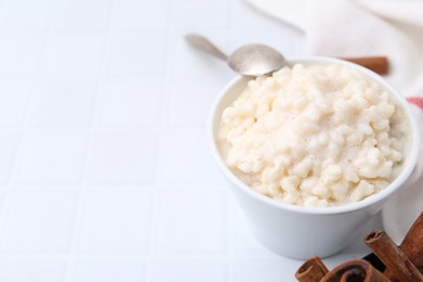 Photo of Tasty rice pudding with cinnamon served on white tiled table, closeup. Space for text