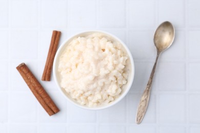 Photo of Tasty rice pudding with cinnamon served on white tiled table, flat lay