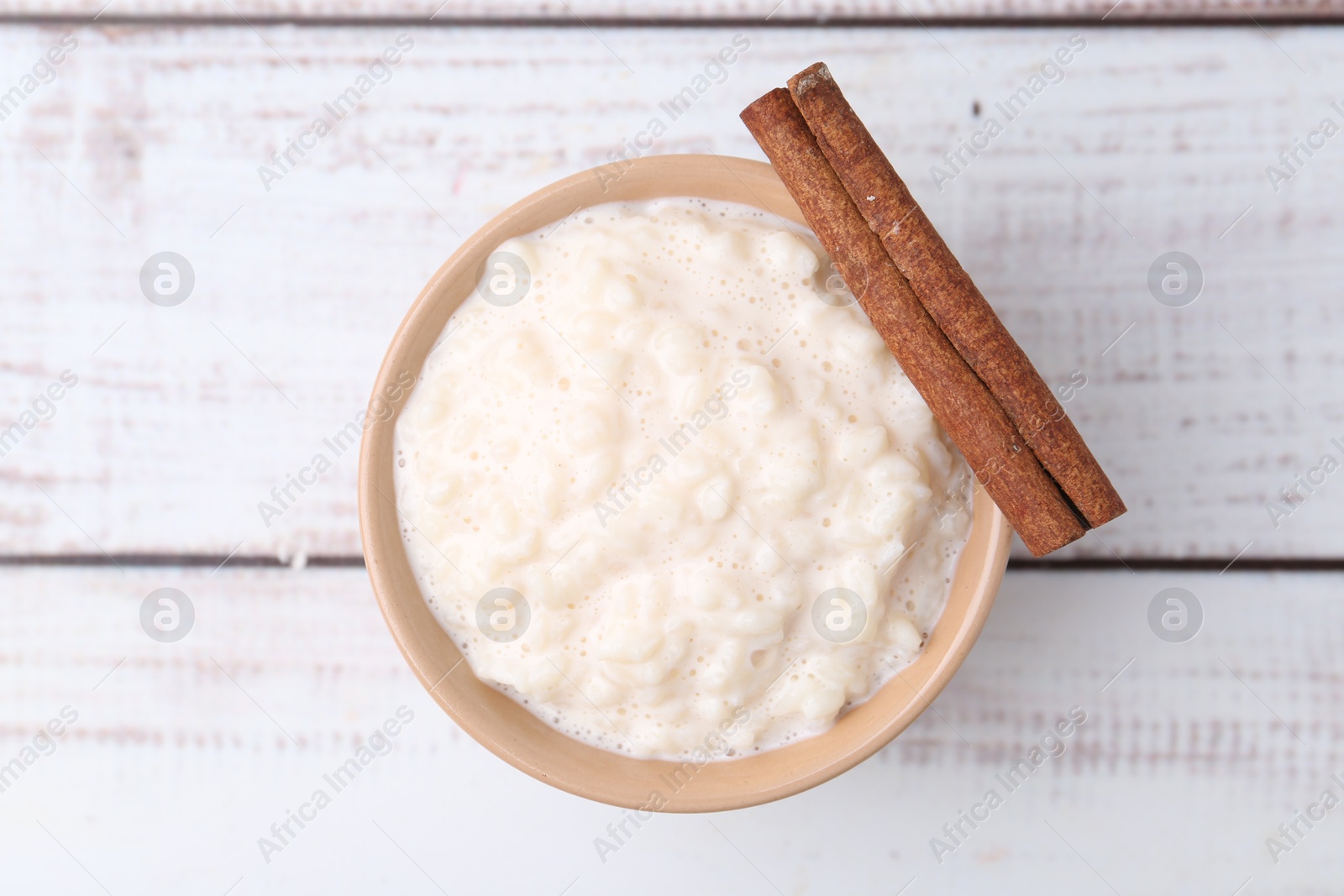 Photo of Tasty rice pudding with cinnamon on white wooden table, top view