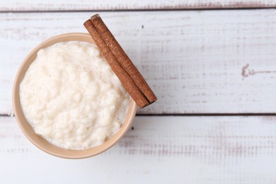 Photo of Tasty rice pudding with cinnamon on white wooden table, top view. Space for text